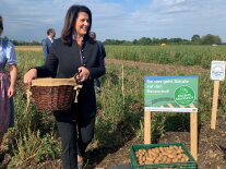 Ministerin Michaela Kaniber auf einem Kartoffelfeld mit einem Korb Kartoffeln. Neben ihr ein Schild zu Erlebnis Bauernhof.