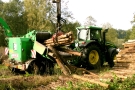 Traktor mit Anhänger zum Zerhacken von Holz. Mittels angebauten Greifarm wird Holz zugeführt.