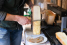Mann schabt warmen Käse auf ein Brot