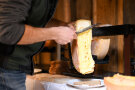 Mann schabt mit Messer warmen Käse auf ein Brot