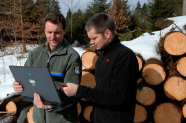Förster mit Laptop berät einen Waldbesitzer vor einem Holzpolter
