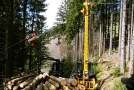 An einen Traktor angebaute Seilkrananlage zieht Holz aus dem Wald und poltert dieses vor sich auf