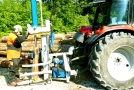 Mittels eines an einen Traktor angebauten Keilspalters bearbeitet ein Waldarbeiter Holz