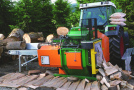 An einem Traktor ist eine Säge-Spalt-Maschine gekoppelt. Rundholz und gespaltenes Holz liegen bereit