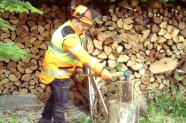 Mann in Schutzkleidung spaltet Holz auf einem Hackstock
