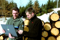 Förster mit Notebook und Waldbesitzer unterhalten sich im Winter vor einem Holzpolter (Foto: C. Hopf)