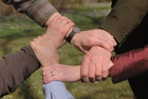 Fünf Menschen halten Hände im Kreis verschränkt